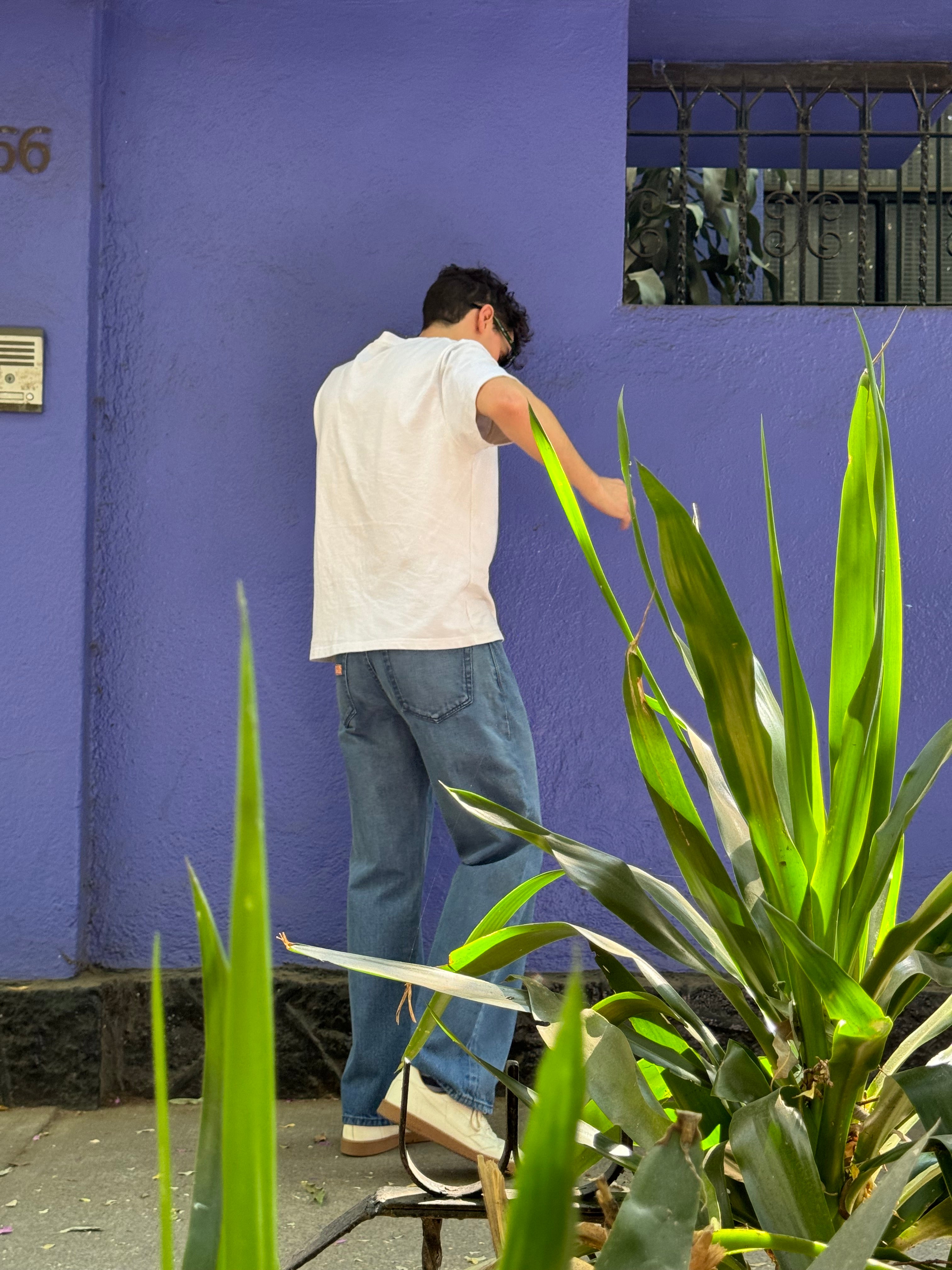 A man standing next to a purple wall with blue jeans and a white t-shirt.