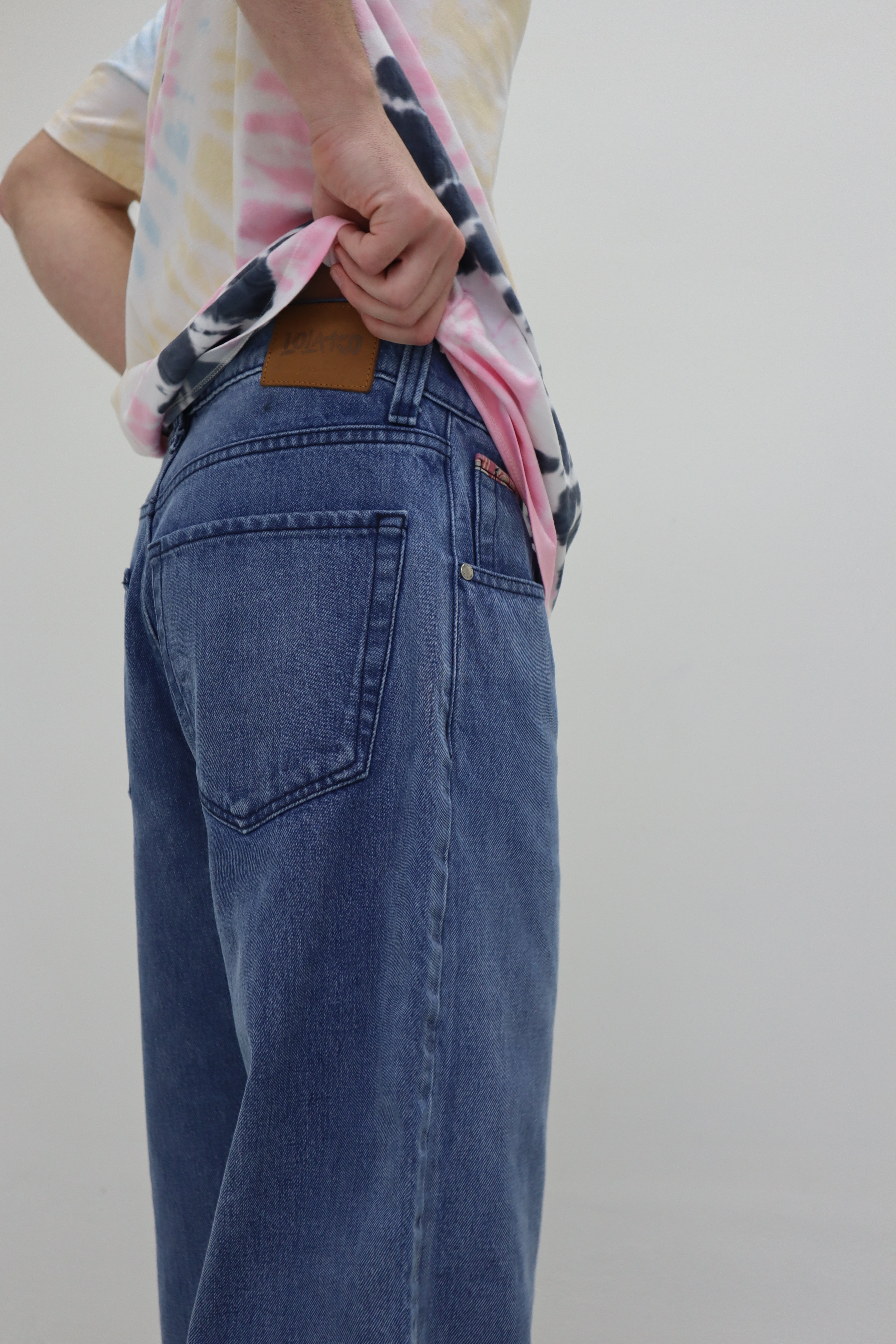 Man in blue jeans with a leather tag displaying the brand name “LOLAKO” and a tie-dye shirt.